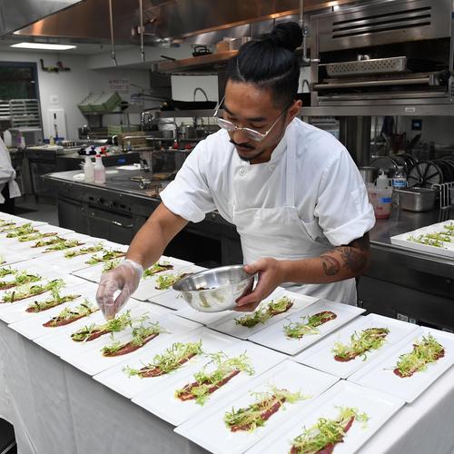 Chef preparing several plates laid out in two rows in a commercial kitchen