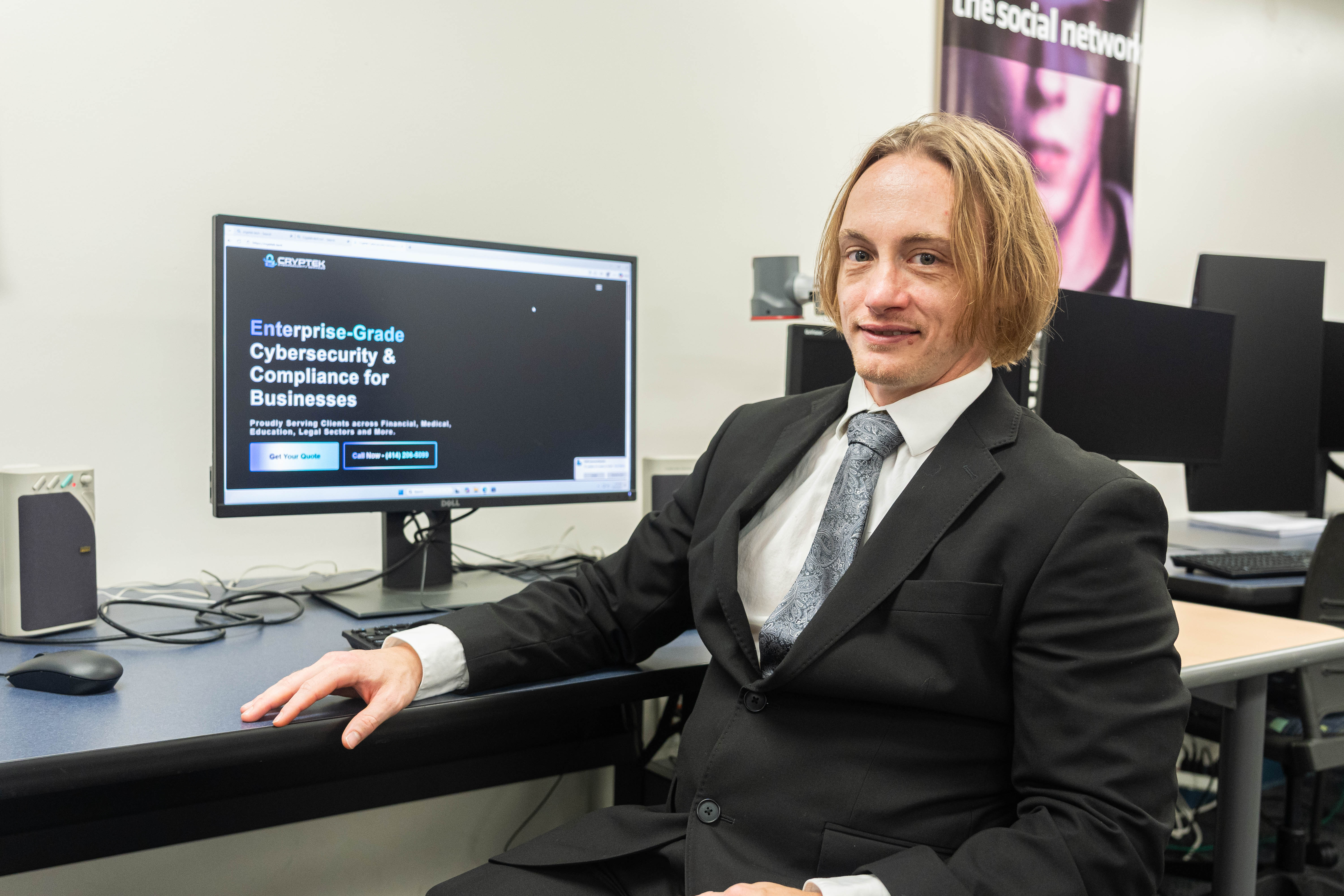James Ballard sitting at a desk smiling at the camera with a computer monitor behind him