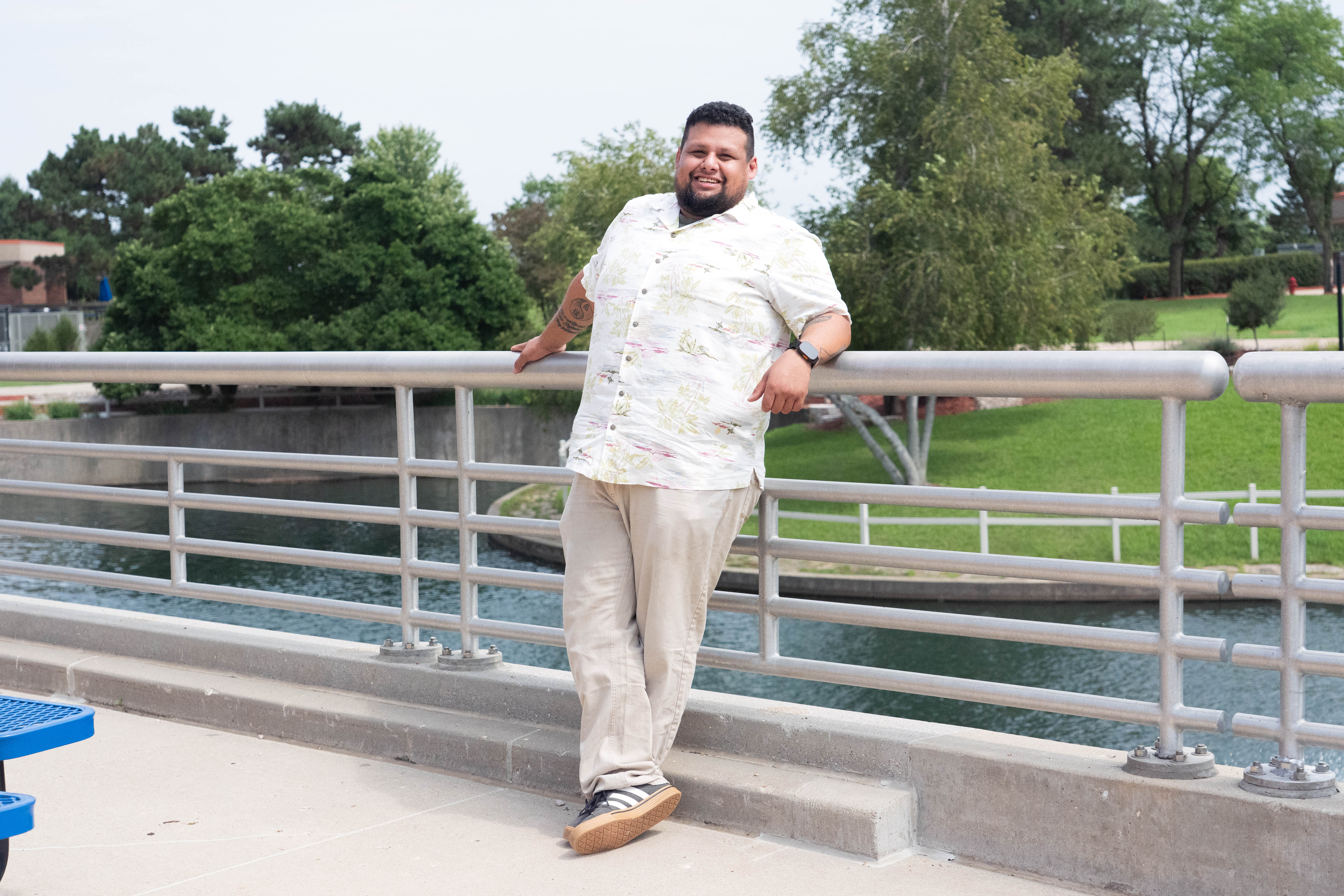 John Molina in a light short-sleeved button down shirt leans back against a railing