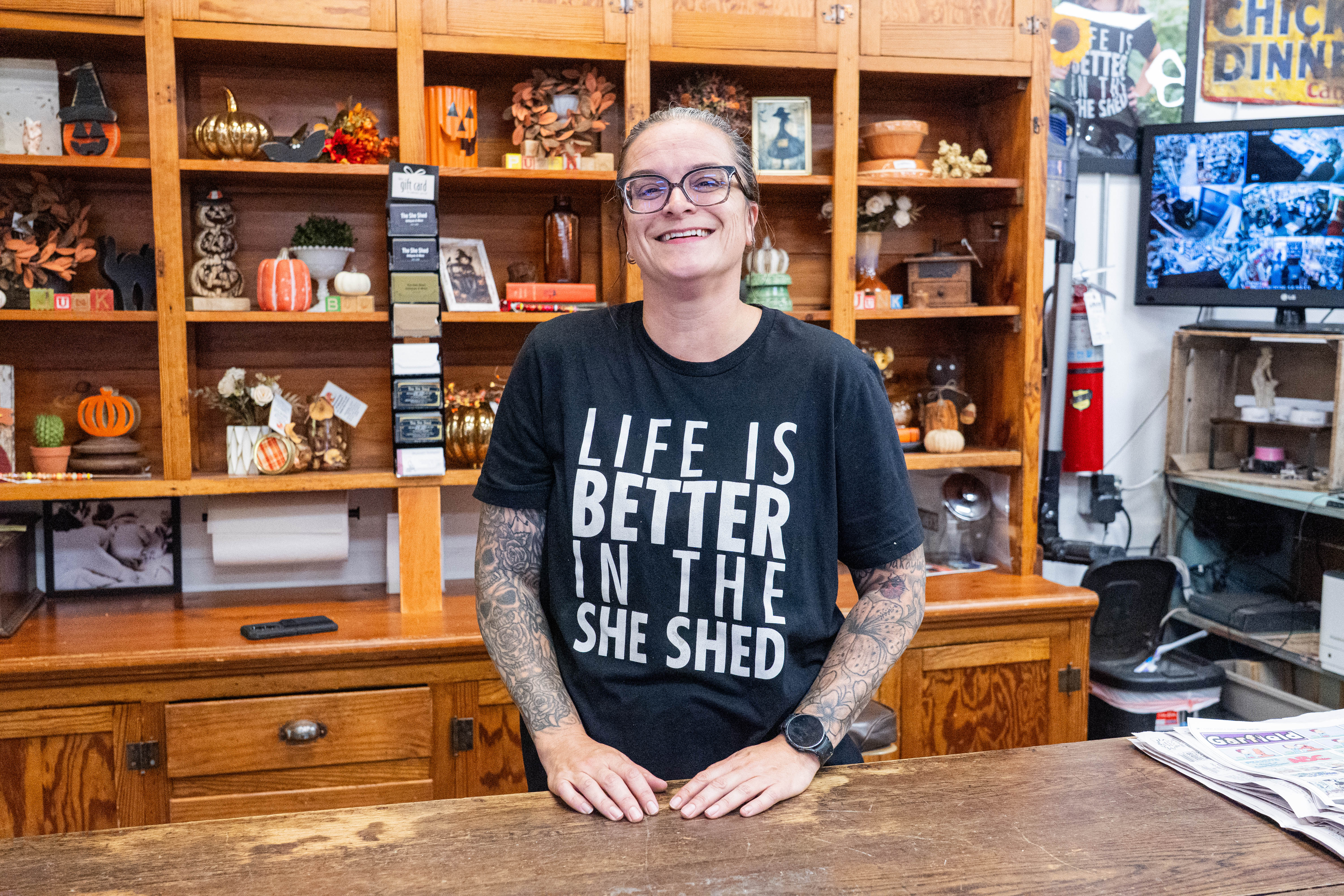 Tricia Orlebeke stands behind the counter at the She Shed with shelves of items behind her.