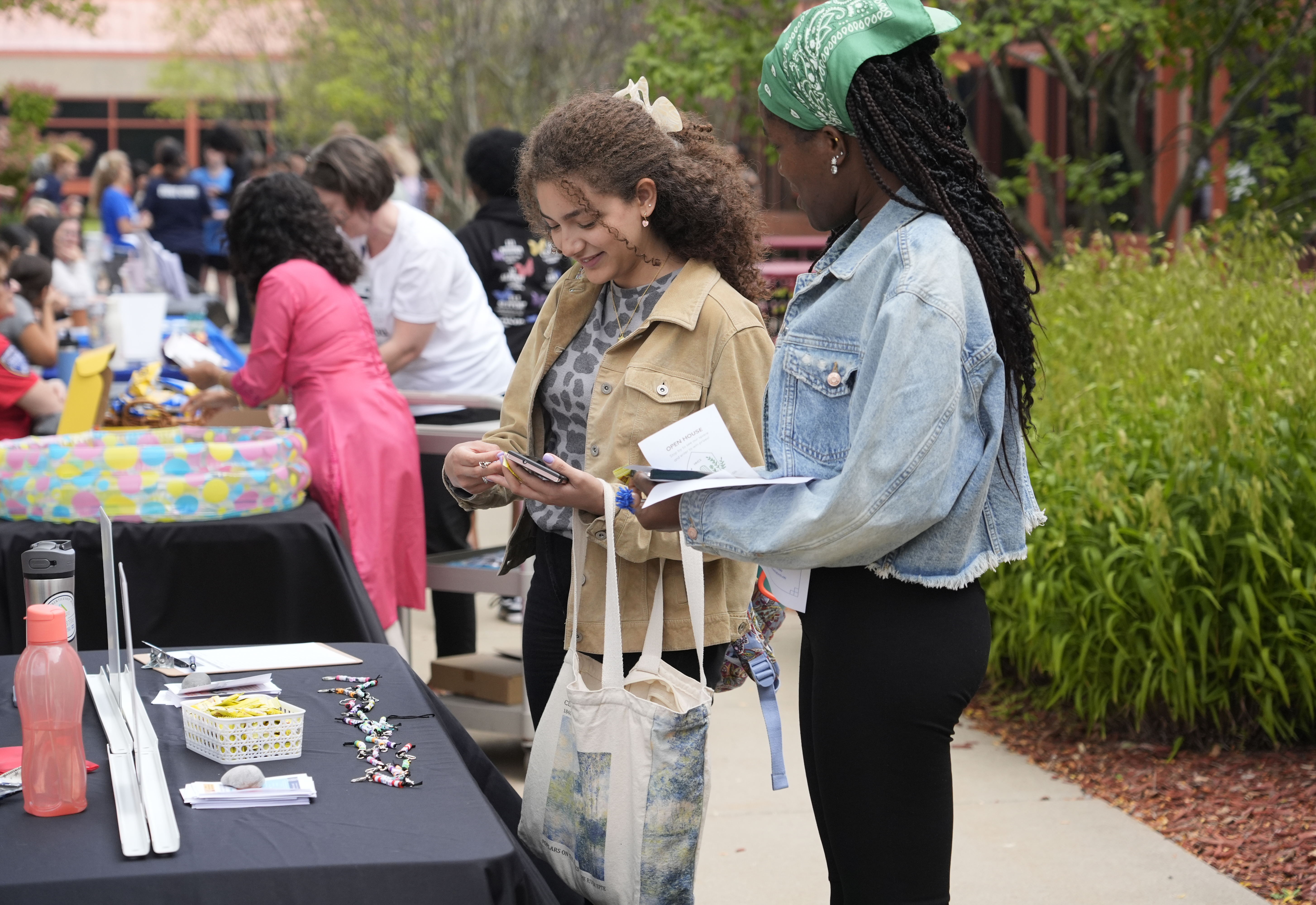 Two students talking with a larger gathering in the background