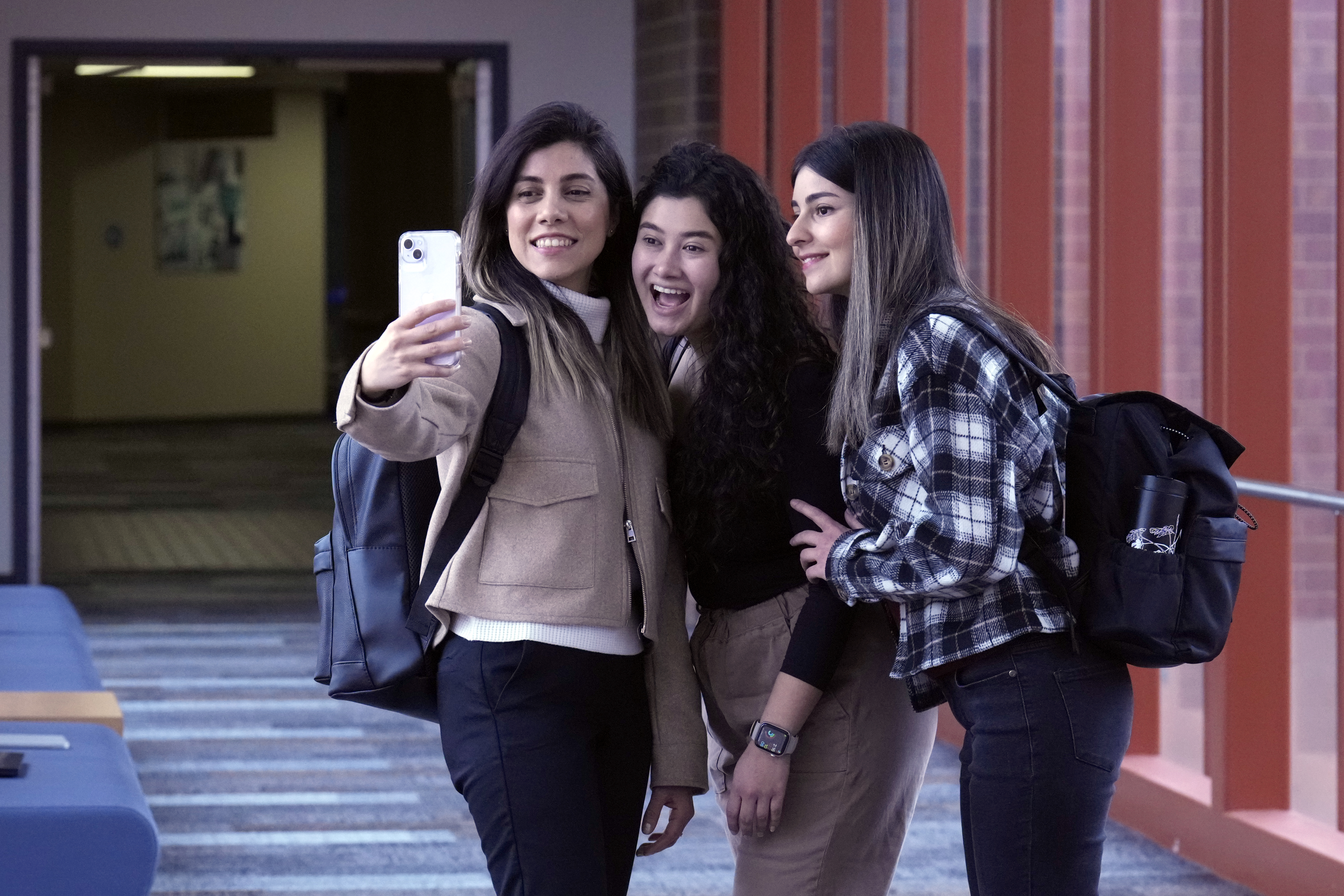 Three female students posing for a selfie together in a well-lit hallway