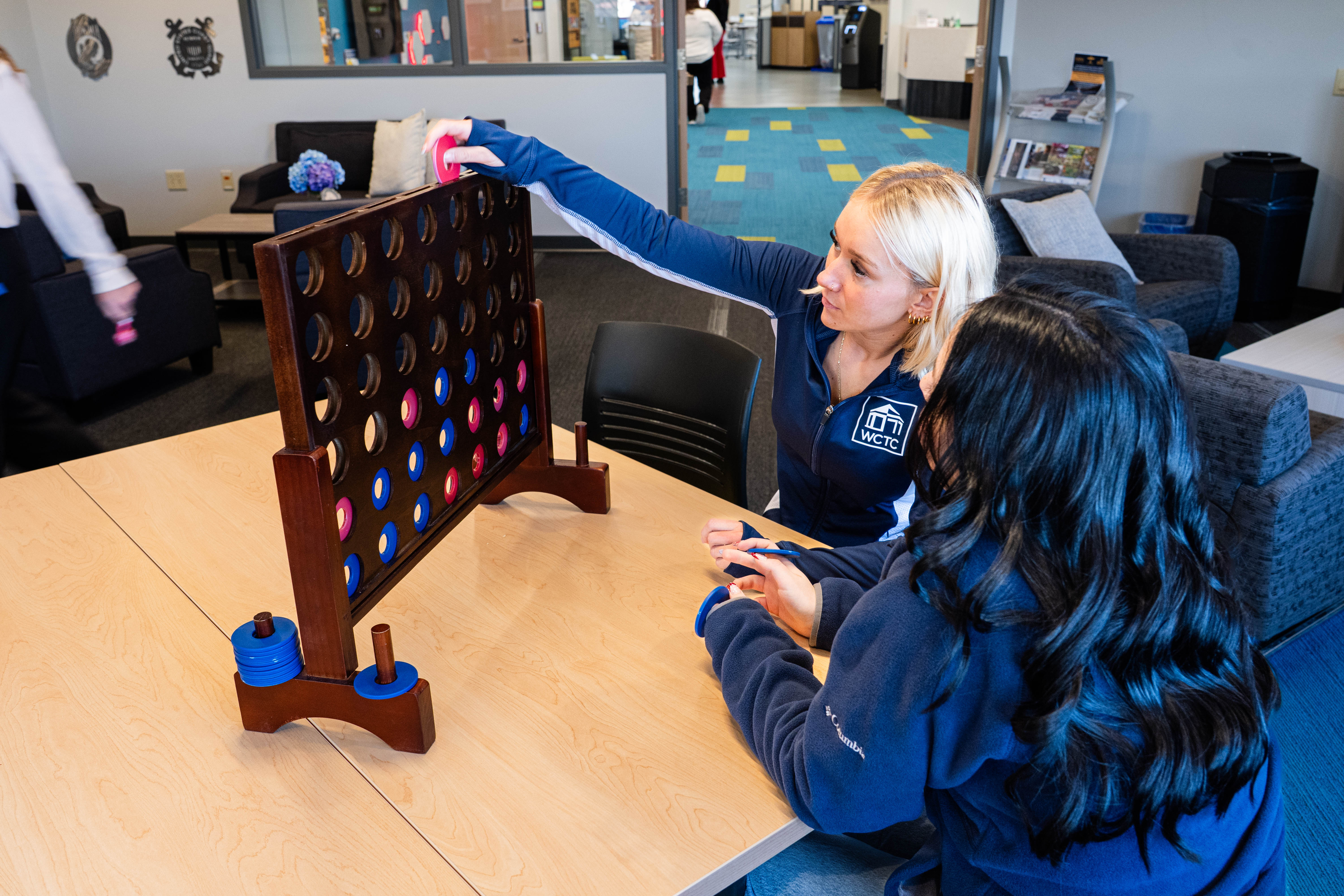 two students sit at a table in the WCTC Student Center playing an oversized game of Connect 4