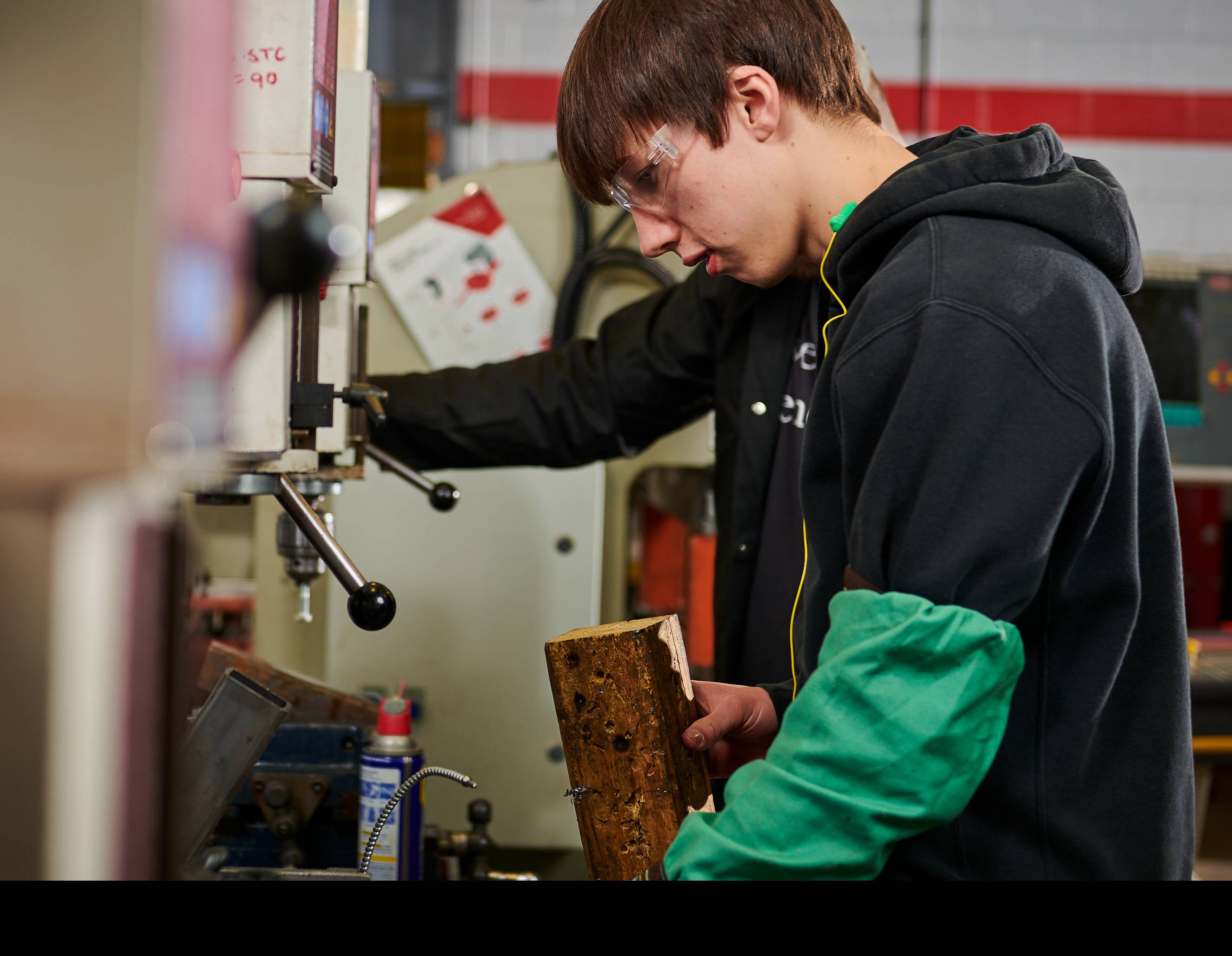 male student in a black hoodie working with manufacturing equipment