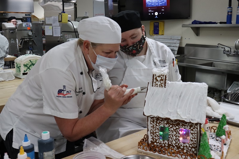 Instructor and student decorating gingerbread house in baking lab